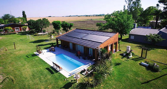 Una casa con un amplio jardín que usa placas solares para calentar el agua de la piscina con energía solar